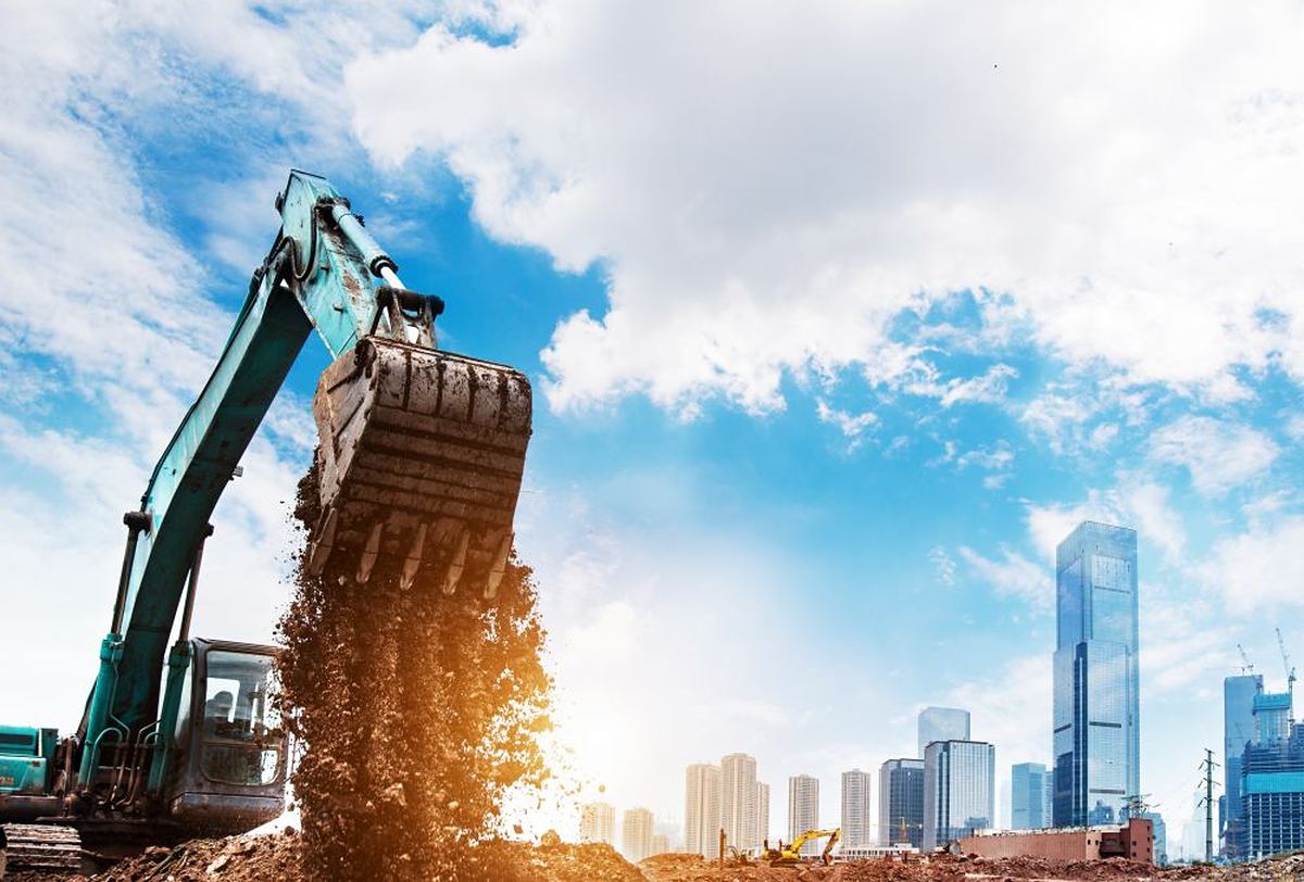 Excavator digging foundations on a construction site with a city skyline behind