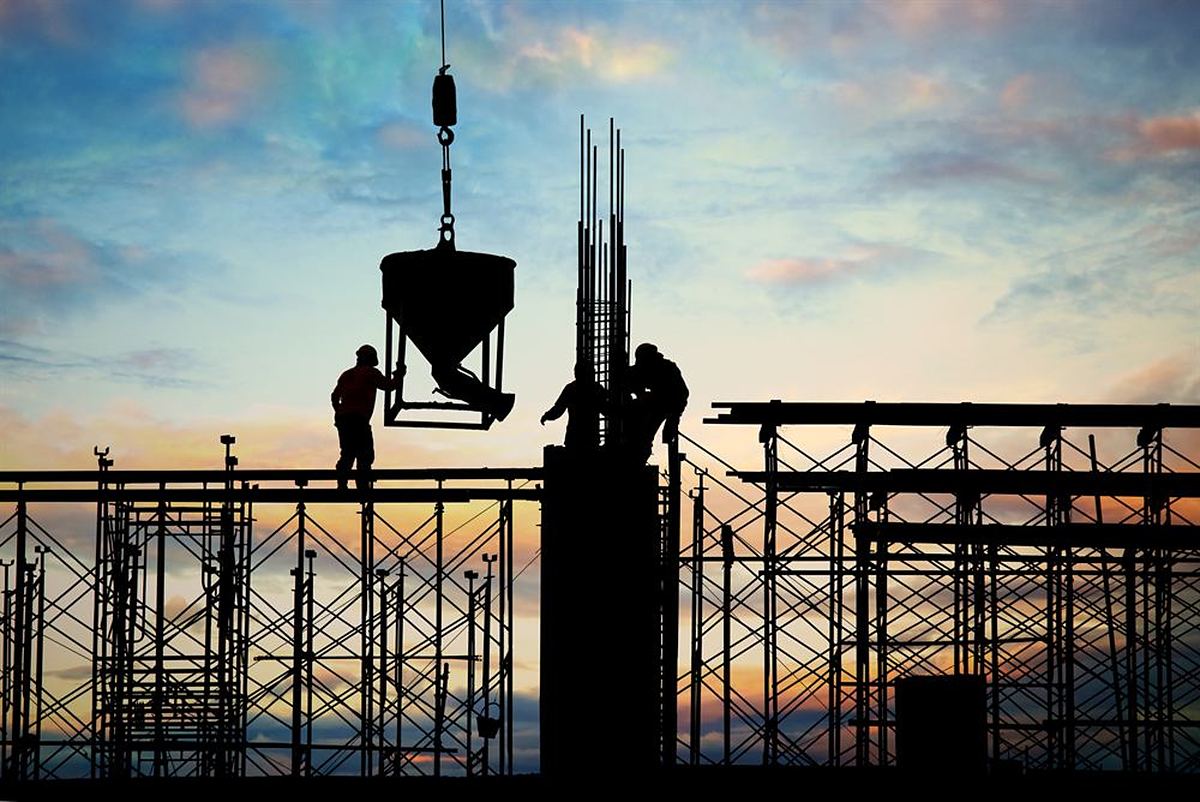 Construction workers silhouetted against a sunset lifting a concrete skip on a building site