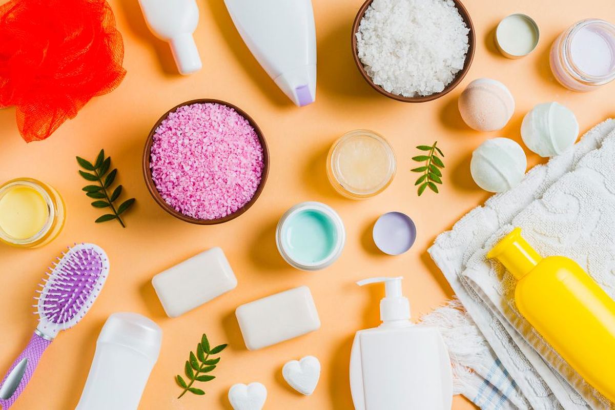 Flat lay of home and personal care products including soap bars, bath salts and bottles on a peach background