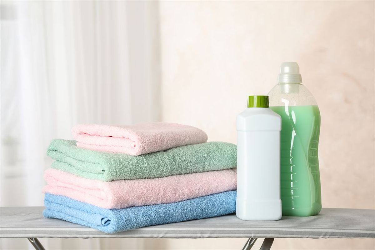 Stack of folded pastel towels beside laundry detergent bottles on an ironing board