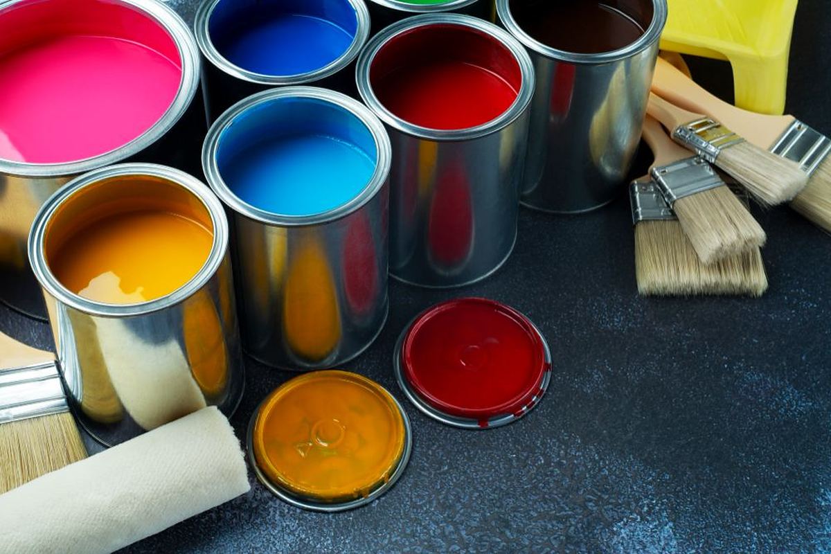 Open cans of brightly coloured paint with brushes on a dark surface