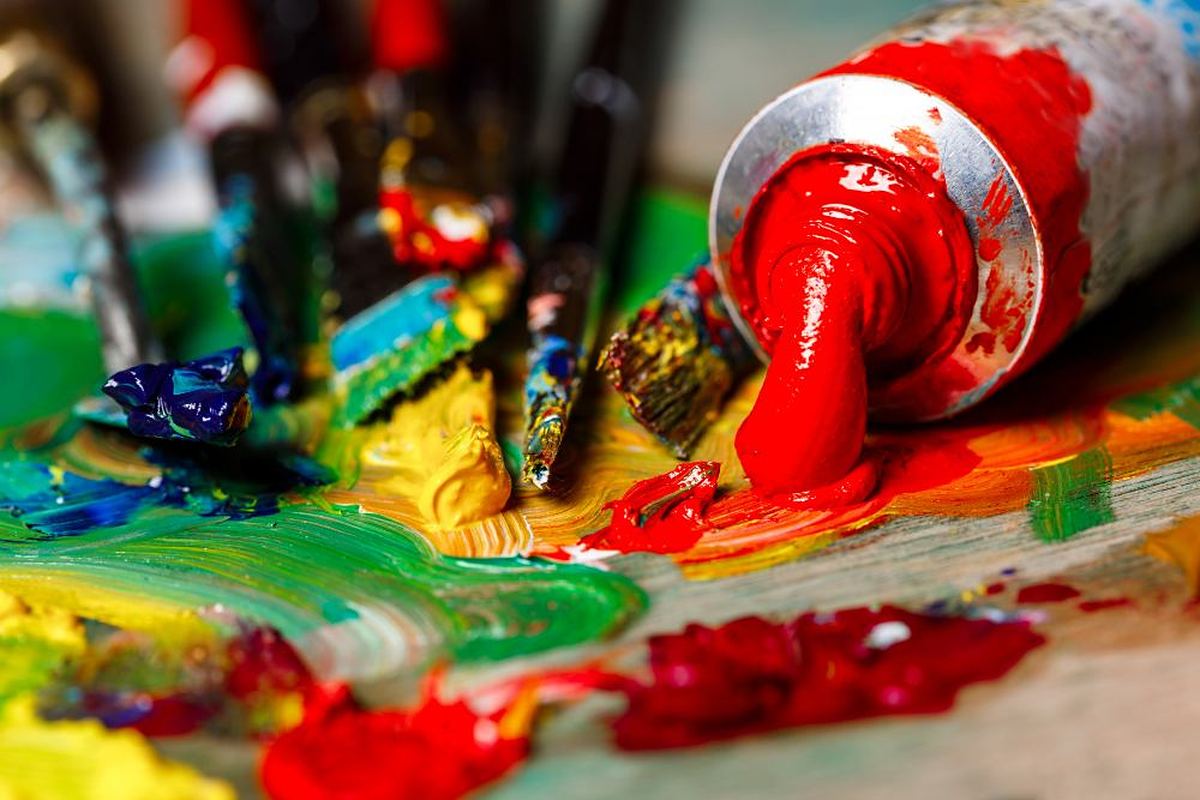 Tube of red paint squeezed onto a palette of mixed colours with artist brushes