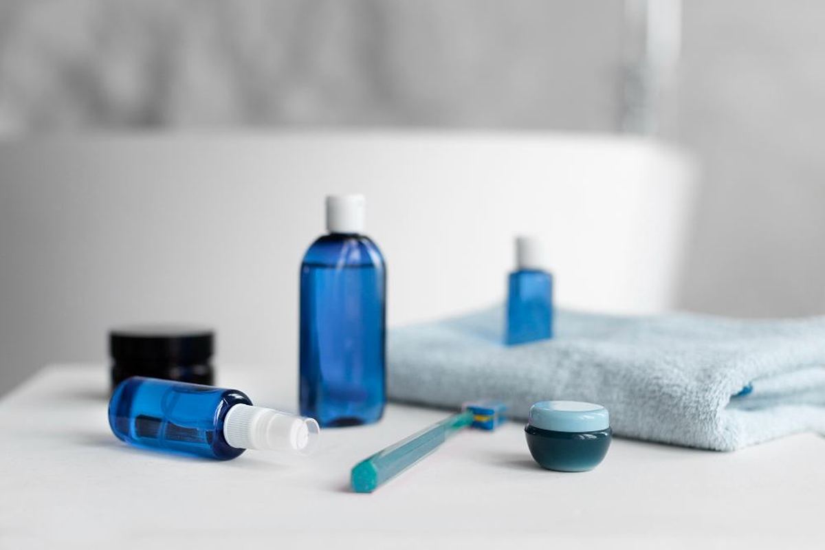 Blue bathroom skincare bottles, jars and a toothbrush arranged on a bathroom surface