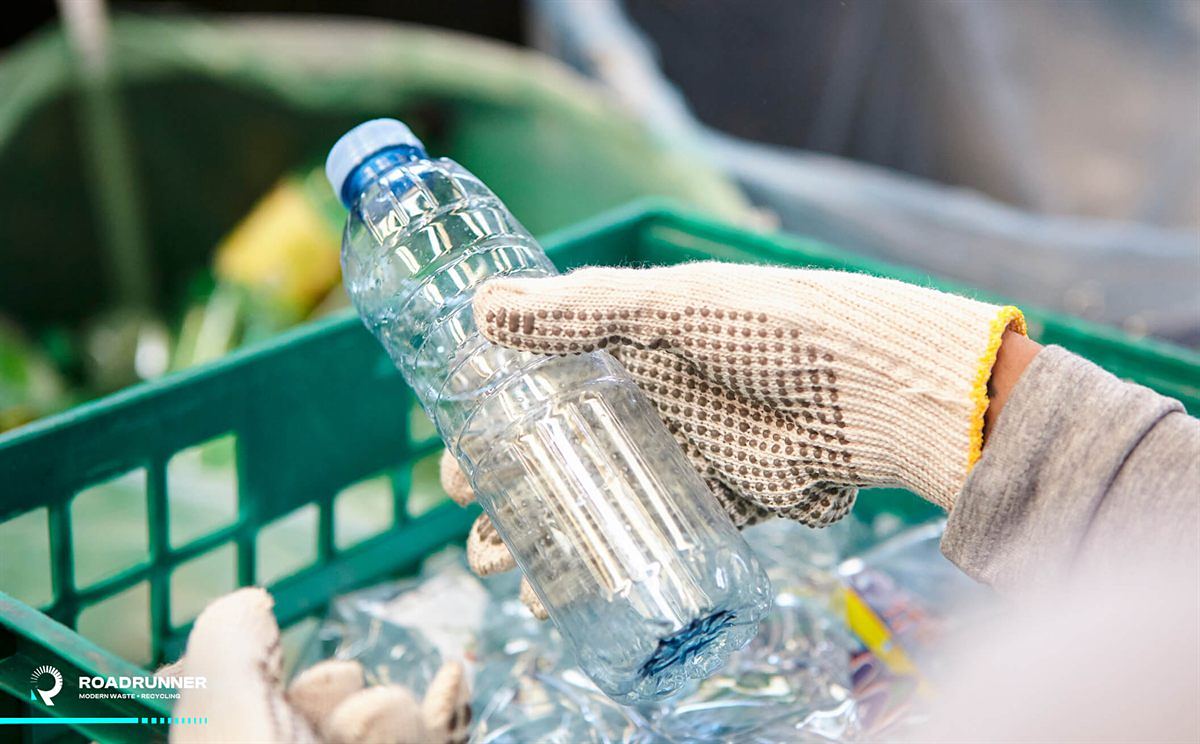 Gloved hand sorting a clear PET bottle into a recycling crate